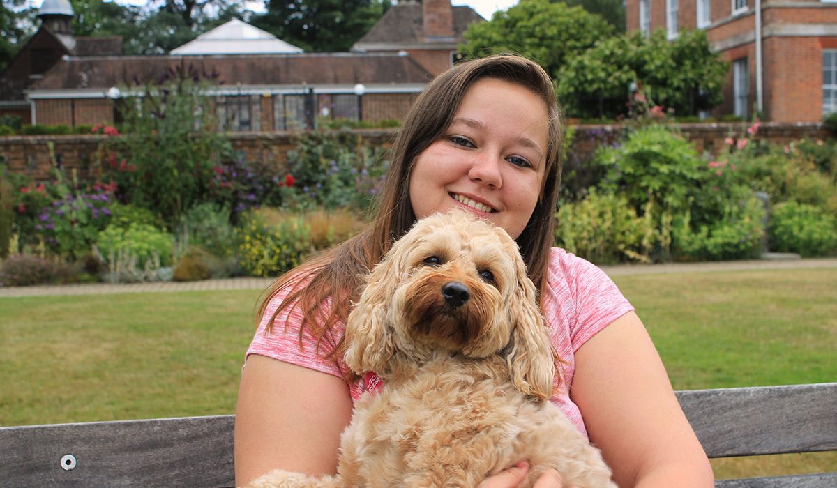 Victoria - on her lap is a blonde, curly haired dog who she is cuddling lovingly.